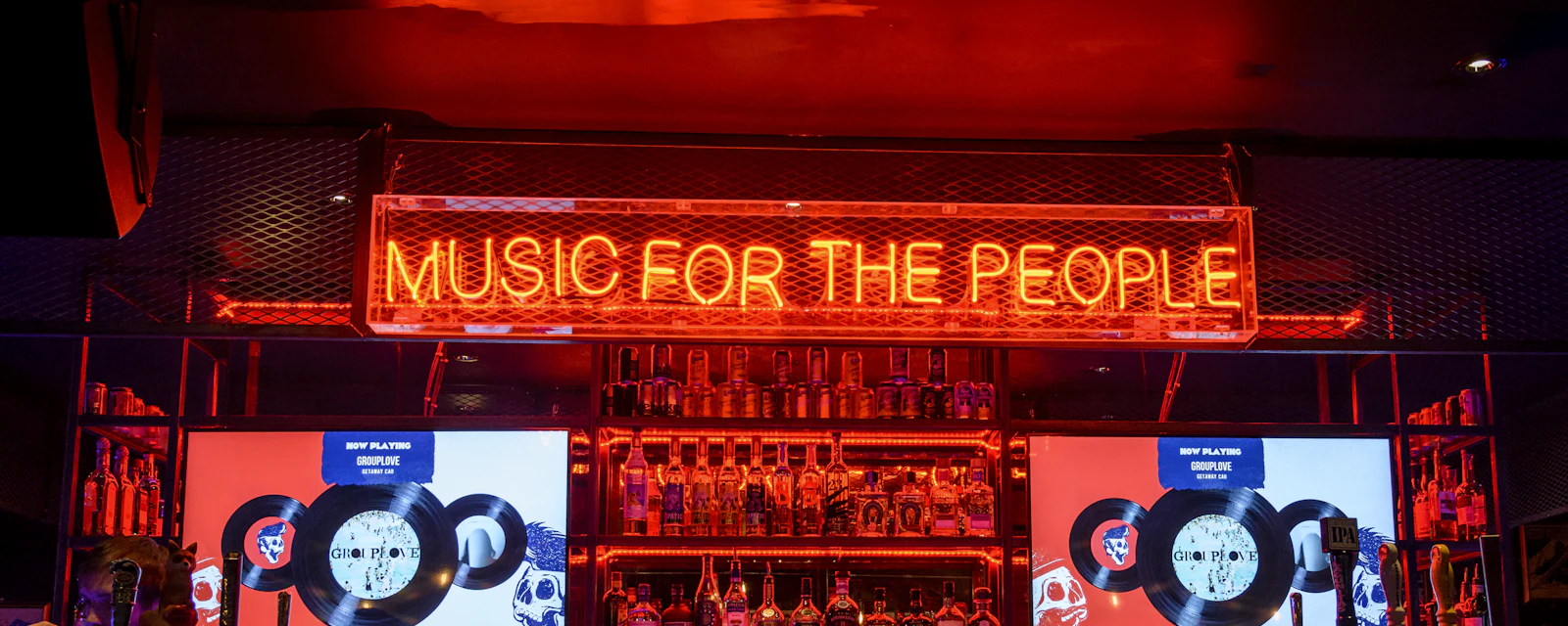 Music for the People neon sign glowing above a fully stocked bar in red light